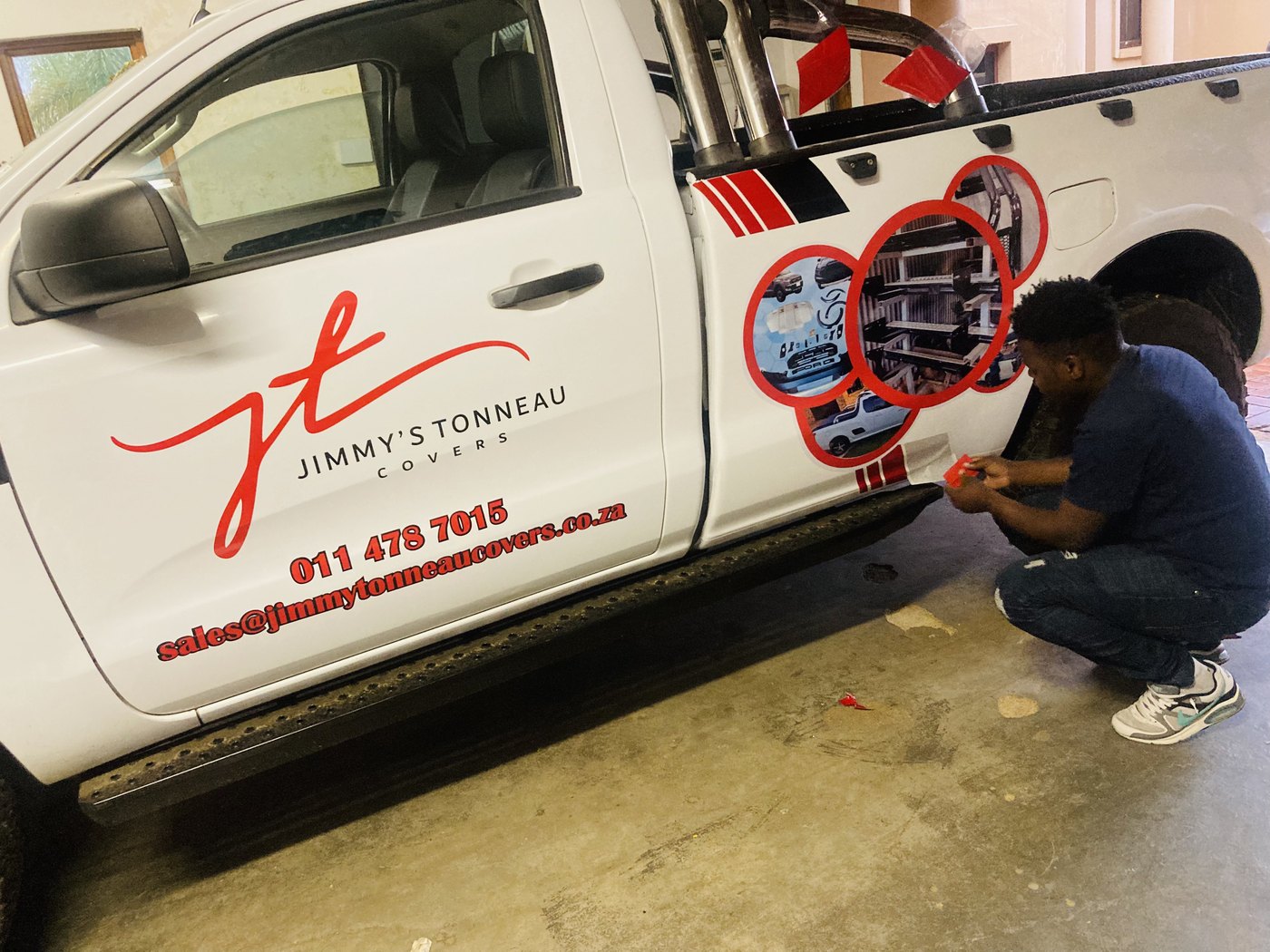 Technician applying vinyl graphics and decals to commercial bakkie